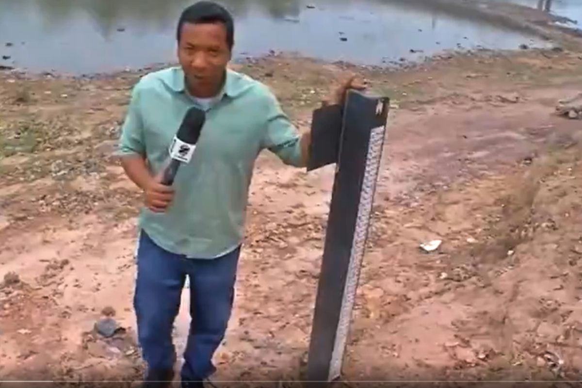 Repórter Jorge Félix ao lado da régua de medição da água no Rio Paraguai. (Foto: TV Centro América)